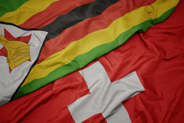 Agitant drapeau coloré de la Suisse et drapeau national de zimbabwe . — Photo