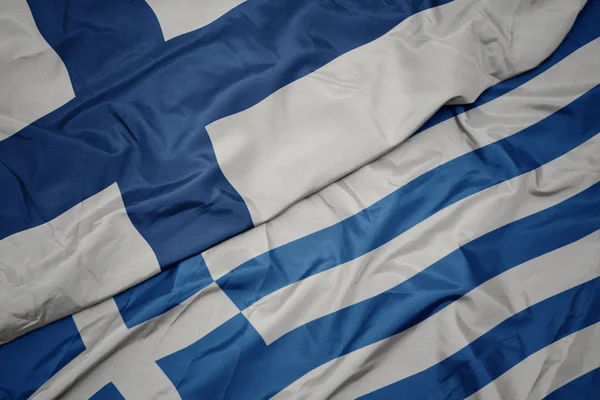 Zwaaiende kleurrijke vlag van Griekenland en de nationale vlag van Finland. — Stockfoto