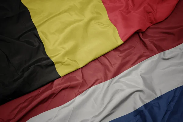 Zwaaiende kleurrijke vlag van Nederland en de nationale vlag van België. — Stockfoto