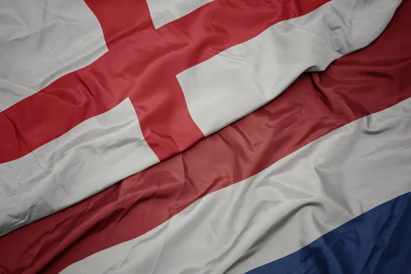 Zwaaiende kleurrijke vlag van Nederland en de nationale vlag van Engeland. — Stockfoto