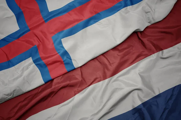 Zwaaiende kleurrijke vlag van Nederland en de nationale vlag van de Faeröer. — Stockfoto