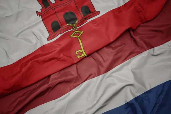 Mávající barevná vlajka Nizozemska a národní vlajky Gibraltaru. — Stock fotografie