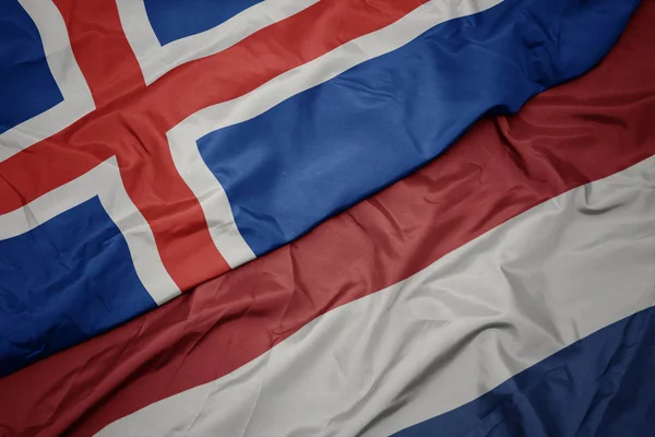 Ondeando colorida bandera de los Países Bajos y bandera nacional de iceland . —  Fotos de Stock