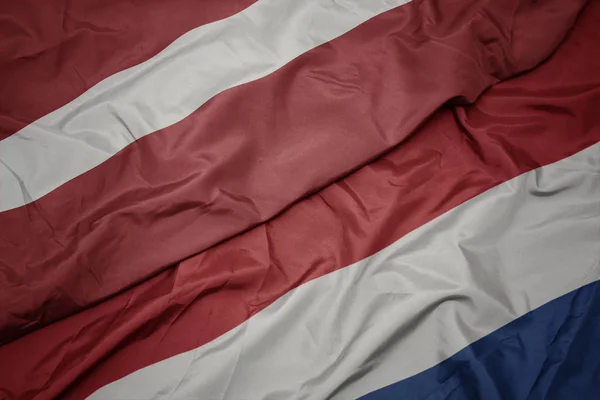 Schwenken bunte Flagge der Niederlande und Nationalflagge Lettlands. — Stockfoto