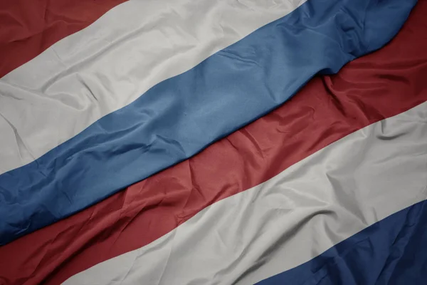 Zwaaiende kleurrijke vlag van Nederland en de nationale vlag van Luxemburg. — Stockfoto