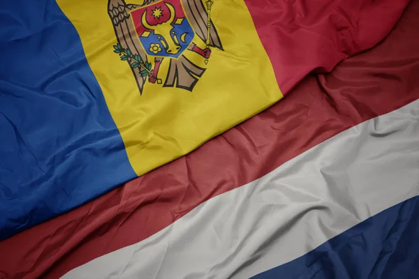 Ondeando colorida bandera de los Países Bajos y bandera nacional de Moldavia . —  Fotos de Stock