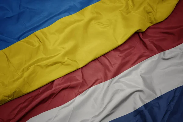 Mávající barvitá vlajka Nizozemska a národní vlajky Ukrajiny. — Stock fotografie