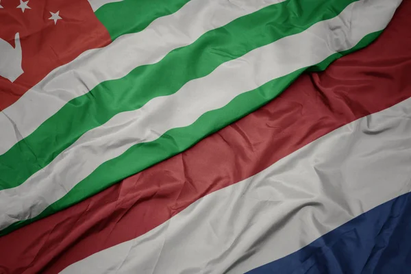 Mávající barvitá vlajka Nizozemska a národní vlajka Abcházie. — Stock fotografie