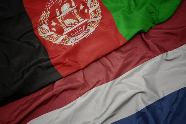 Ondeando colorida bandera de los Países Bajos y bandera nacional de Afganistán . — Foto de Stock