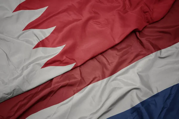 waving colorful flag of netherlands and national flag of bahrain.
