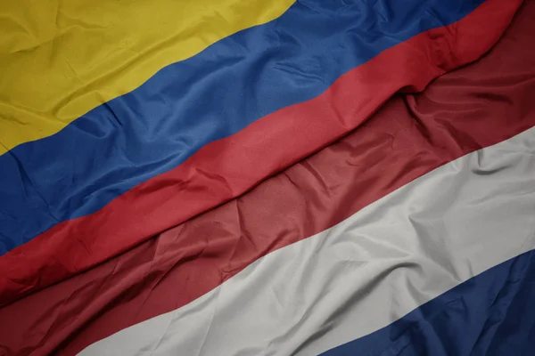 Ondeando colorida bandera de los Países Bajos y bandera nacional de Colombia . —  Fotos de Stock