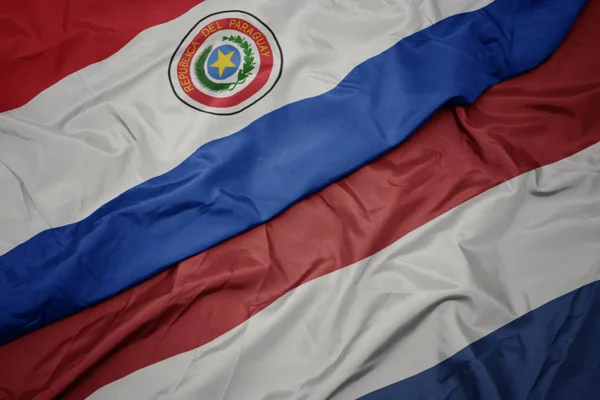 Zwaaiende kleurrijke vlag van Nederland en de nationale vlag van Paraguay. — Stockfoto