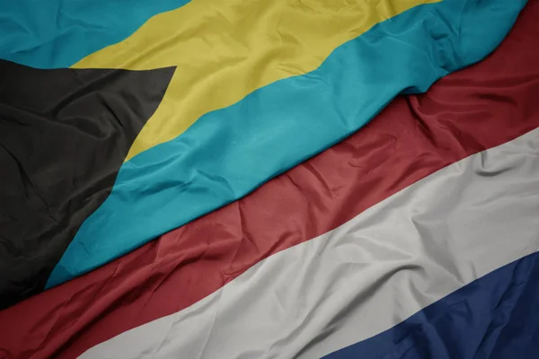 Mávající barvitá vlajka Nizozemska a národní vlajka Baham. — Stock fotografie