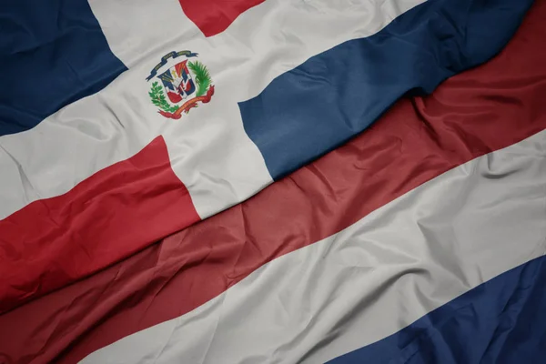 Ondeando colorida bandera de los Países Bajos y bandera nacional de la República Dominicana . — Foto de Stock