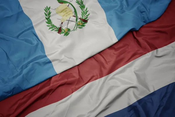 Ondeando colorida bandera de los Países Bajos y bandera nacional de guatemala . —  Fotos de Stock