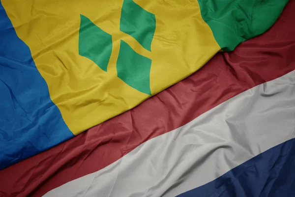 Mávající barvitá vlajka Nizozemska a národní vlajka svatého Vincenta a Grenadiny. — Stock fotografie