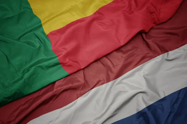 Mávající barvitá vlajka Nizozemska a národní vlajka Benin. — Stock fotografie