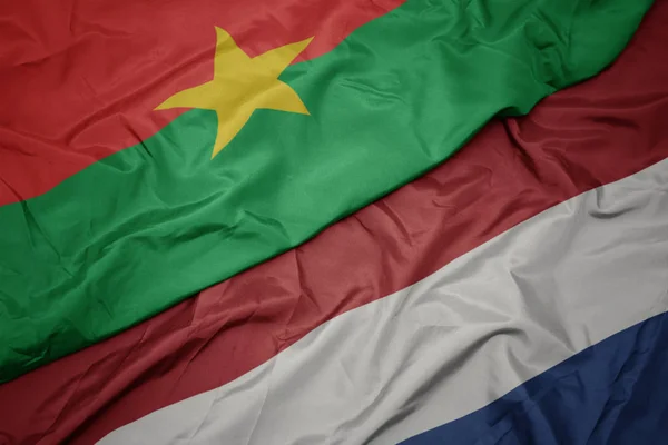Mávající barevná vlajka Nizozemska a národní vlajka Burkina Faso. — Stock fotografie