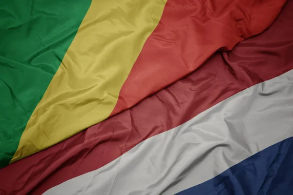 Mávající barvitá vlajka Nizozemska a národní vlajka republiky Kongo. — Stock fotografie