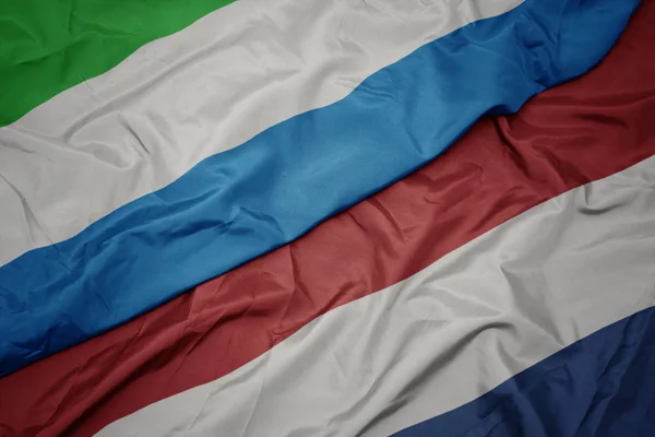 Mávající barvitá vlajka Nizozemska a národní vlajka Sierry Leone. — Stock fotografie