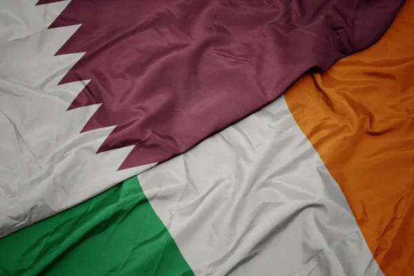 Waving colorful flag of ireland and national flag of qatar. — Stock Photo, Image