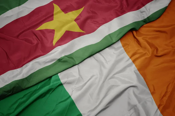 Ondeando colorida bandera de Irlanda y bandera nacional de Surinam . — Foto de Stock