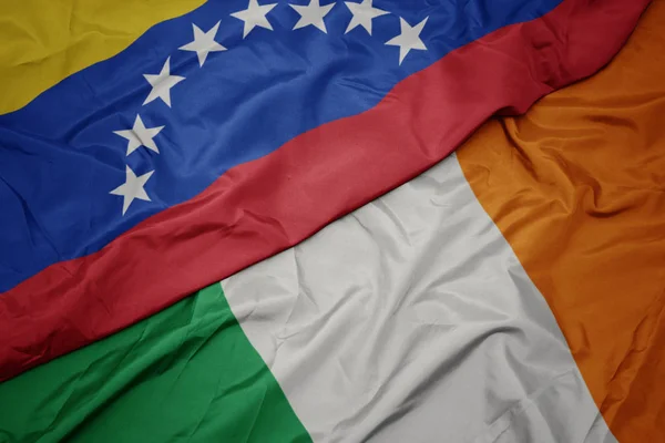 Waving colorful flag of ireland and national flag of venezuela. — Stock Photo, Image