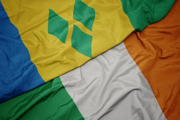 Zwaaiende kleurrijke vlag van Ierland en de nationale vlag van Saint Vincent en de Grenadines. — Stockfoto