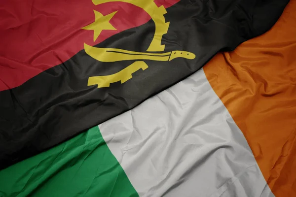 Ondeando colorida bandera de Irlanda y bandera nacional de Angola . —  Fotos de Stock