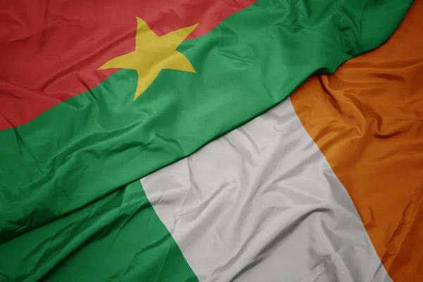 Ondeando colorida bandera de Irlanda y bandera nacional de Burkina faso . — Foto de Stock