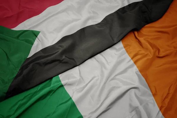Schwenken bunte Flagge Irlands und Nationalflagge Sudans. — Stockfoto