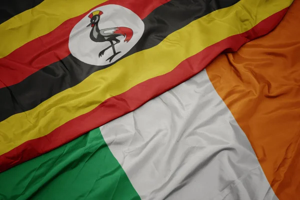 Waving colorful flag of ireland and national flag of uganda — Stock Photo, Image