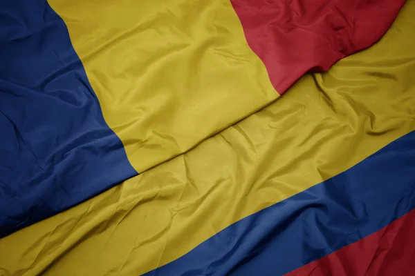 Zwaaiende kleurrijke vlag van Colombia en de nationale vlag van Roemenië. — Stockfoto