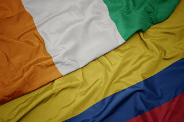 Agitant le drapeau coloré de la colombie et le drapeau national de cote divoire . — Photo