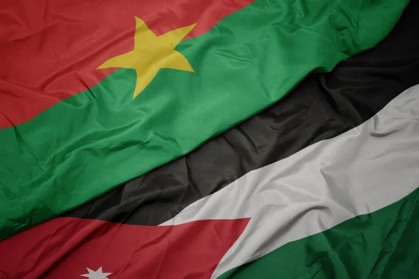 Ondeando colorida bandera de Jordania y bandera nacional de Burkina faso . — Foto de Stock