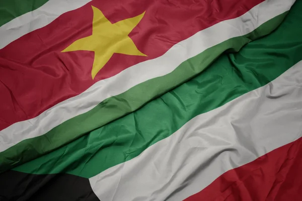 Ondeando colorida bandera de kuwait y bandera nacional de surinam . — Foto de Stock