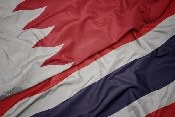 waving colorful flag of thailand and national flag of bahrain.