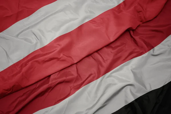 Zwaaiende kleurrijke vlag van Jemen en de nationale vlag van Oostenrijk. — Stockfoto