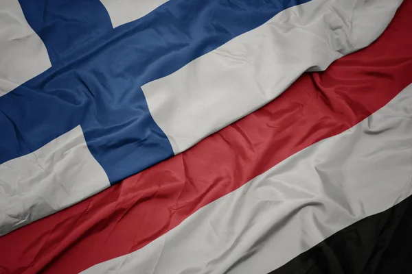 Schwenken bunte Flagge des Jemen und Nationalflagge Finnlands. — Stockfoto