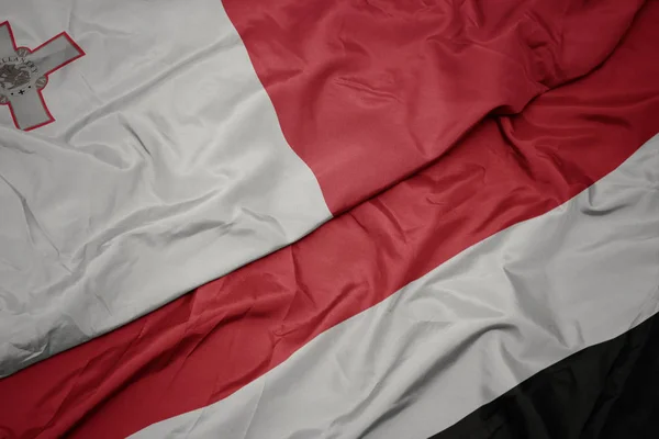 Zwaaiende kleurrijke vlag van Jemen en de nationale vlag van Malta. — Stockfoto