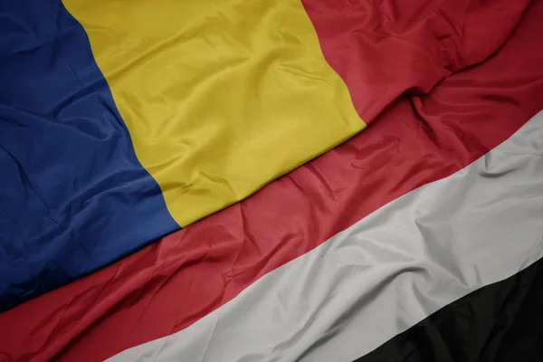 Waving colorful flag of yemen and national flag of romania. — Stock Photo, Image