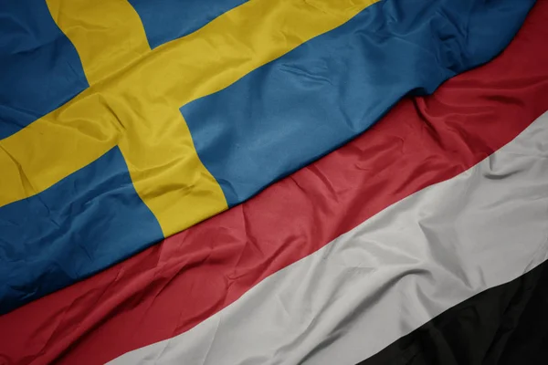 Melambaikan bendera berwarna-warni yemen dan bendera nasional sweden . — Stok Foto