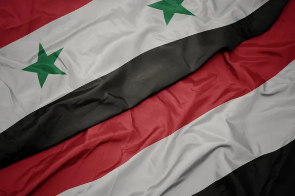 Zwaaiende kleurrijke vlag van Jemen en de nationale vlag van Syrië. — Stockfoto