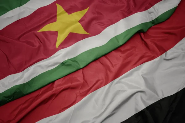 Ondeando colorida bandera de yemen y bandera nacional de surinam . — Foto de Stock