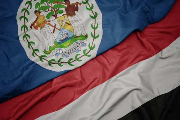 Zwaaiende kleurrijke vlag van Jemen en de nationale vlag van Belize. — Stockfoto