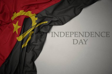 metin bağımsızlık günü ile gri bir arka plan üzerinde angola renkli ulusal bayrak sallayarak.