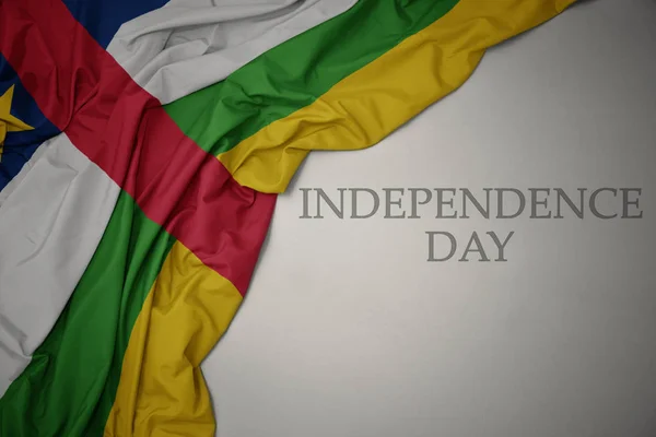 Machając kolorowe flagi narodowej Republiki Środkowoafrykańskiej na szarym tle Dzień Niepodległości tekstu. — Zdjęcie stockowe