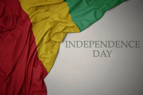 Machając kolorowe flagi narodowej Gwinei na szarym tle z dniem niepodległości tekstu. — Zdjęcie stockowe