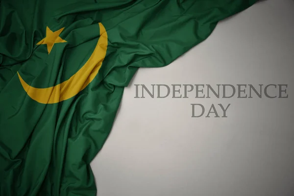 Ondeando colorida bandera nacional de Mauritania sobre un fondo gris con el día de la independencia del texto . — Foto de Stock