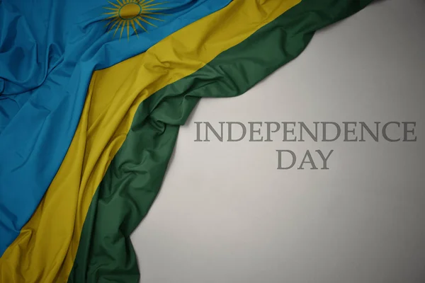 Schwenken bunte Nationalflagge Ruandas auf grauem Hintergrund mit Text zum Unabhängigkeitstag. — Stockfoto
